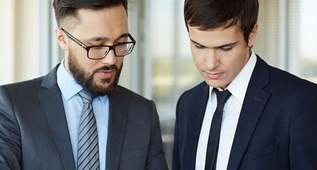 Two men both wearing suits look down at something off camera.