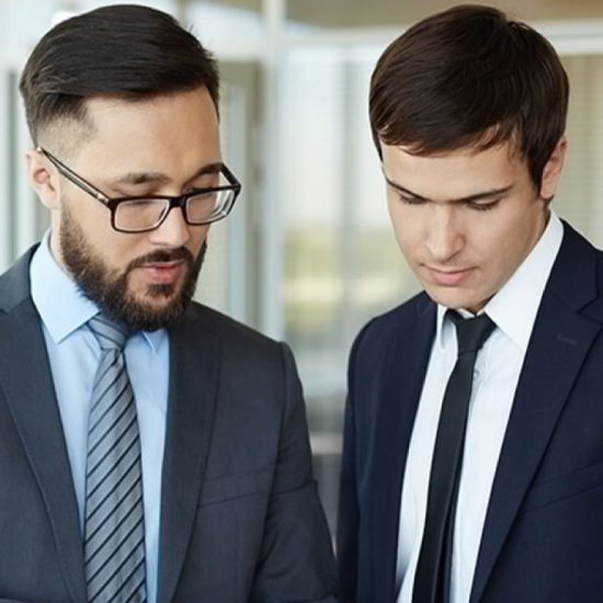 Two men both wearing suits look down at something off camera.