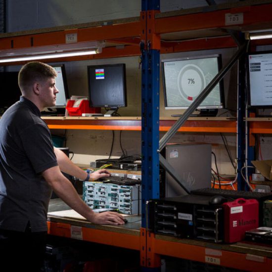 A man wearing a dark polo shirt stands in front of several screens.