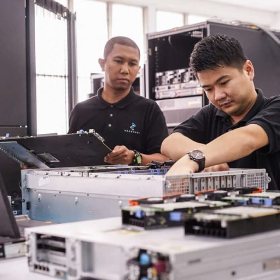 Two male employees dressed in black polo shirts with the Procurri logo reach inside electrical equipment.