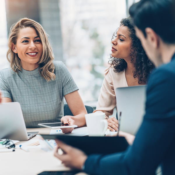 Two women and a man smartly dressed sit around a desk smiling.