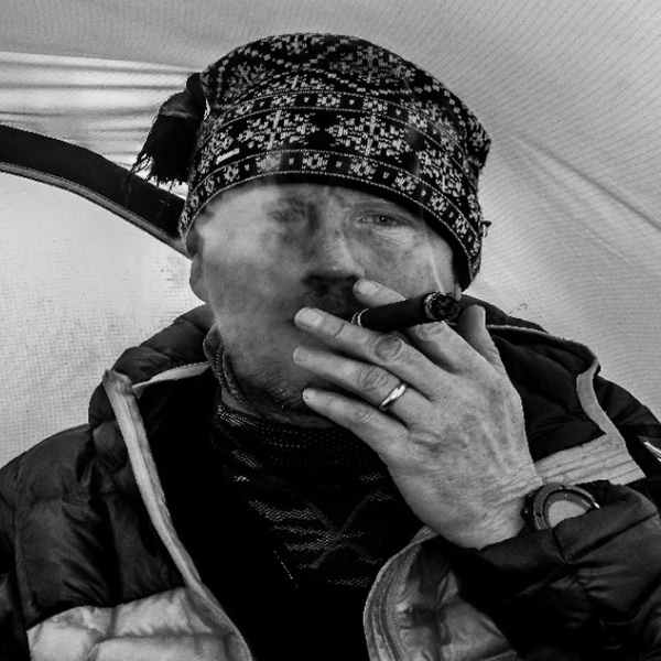 A close-up black and white photo of a man wearing a beanie hat vaping.