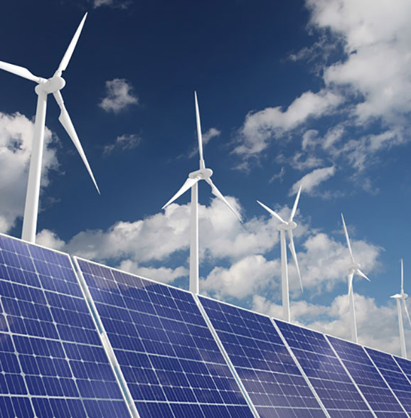 A photo of solar panels with wind turbines and a sunny blue sky above.