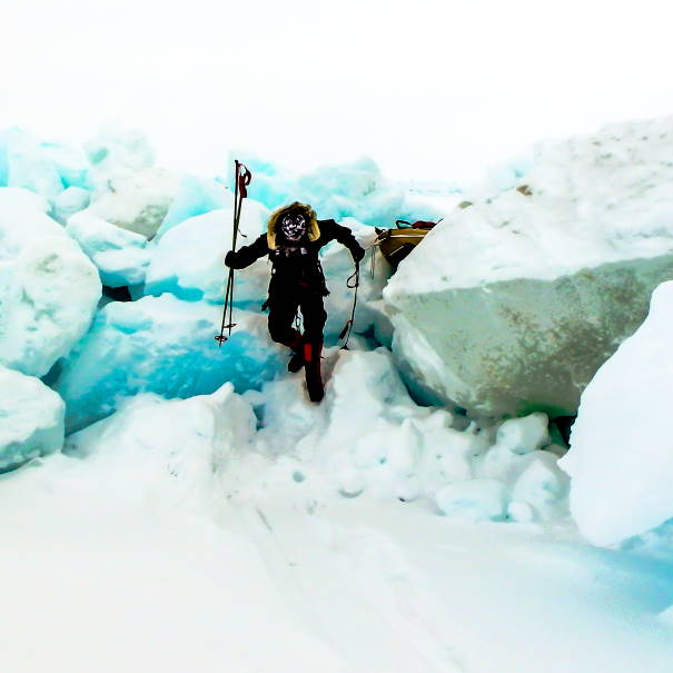A photo of Paul Vicary in full cold weather regalia climbing over an ice rift.