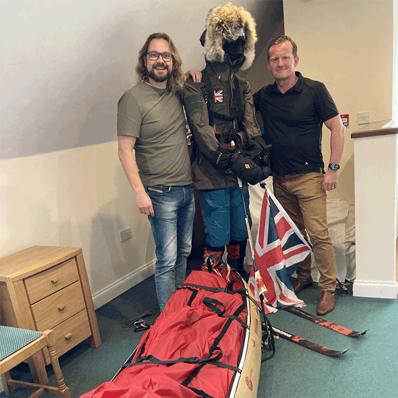 Two men stand next to a mannequin wearing warm thermal clothing and skis.