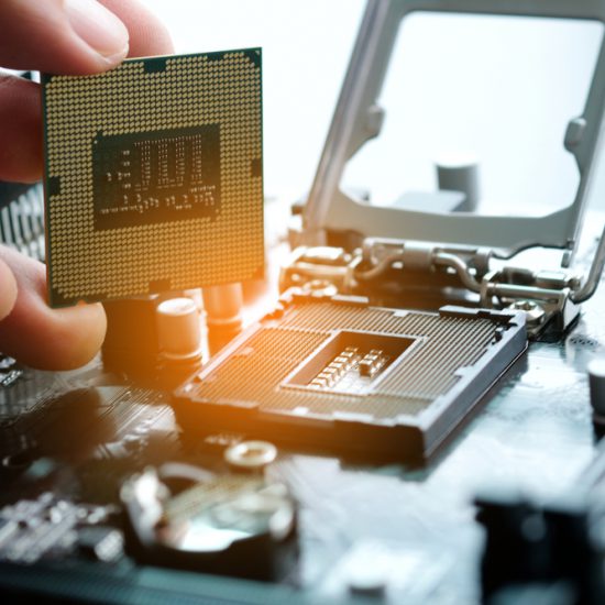 A hand holds up a computer chip above other computing hardware.