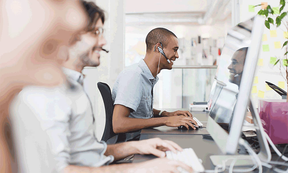 A row of three adults sitting in front of computers wearing headphones look at their computer screens.
