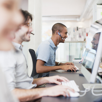 ps-1 Eine Reihe von drei Erwachsenen sitzt mit Kopfhörern vor Computern und schaut auf ihre Bildschirme.
